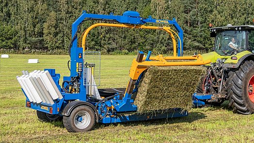 Met de balenopnemer wordt de vierkante baal op de wikkeltafel getild.