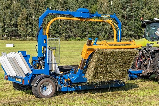 Met de balenopnemer wordt de vierkante baal op de wikkeltafel getild.