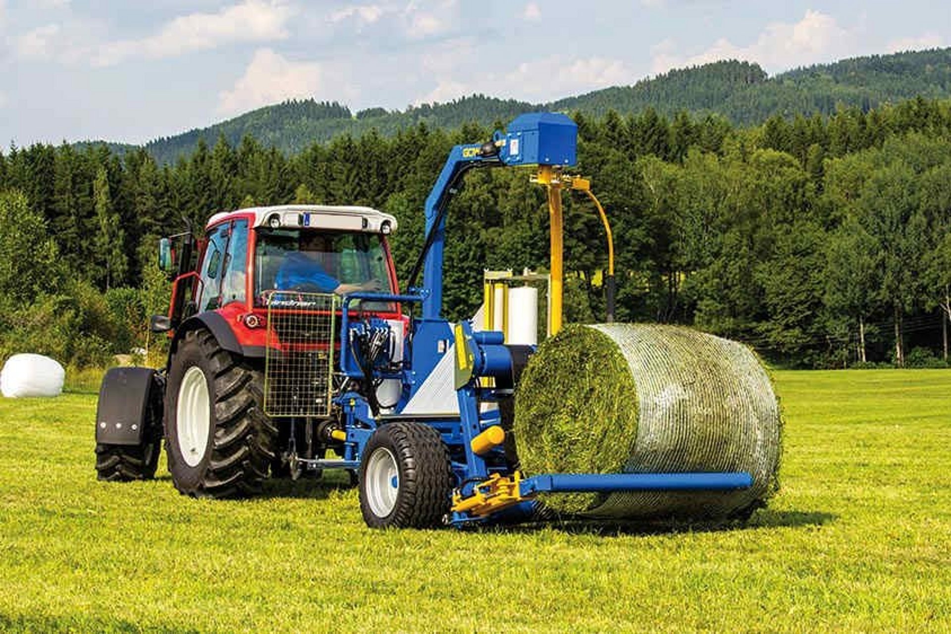 De hydraulische laadarm pakt de baal op en legt deze op de wikkeltafel.
